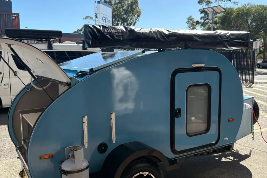 Sky blue compact Breath teardrop with rear hatch open, roof solar panel and awning bag