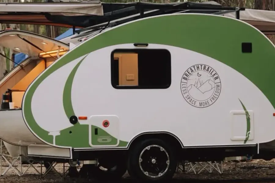 Breath Max in green and white set up at a bush campsite with awning out and rear galley lit