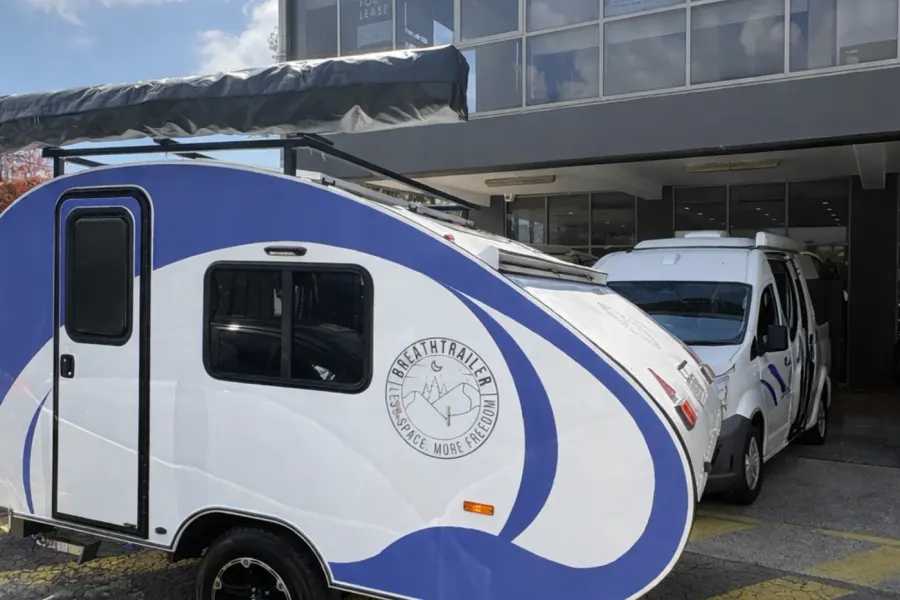 Breath Max in blue and white with roof rack and awning bag parked in front of a commercial building