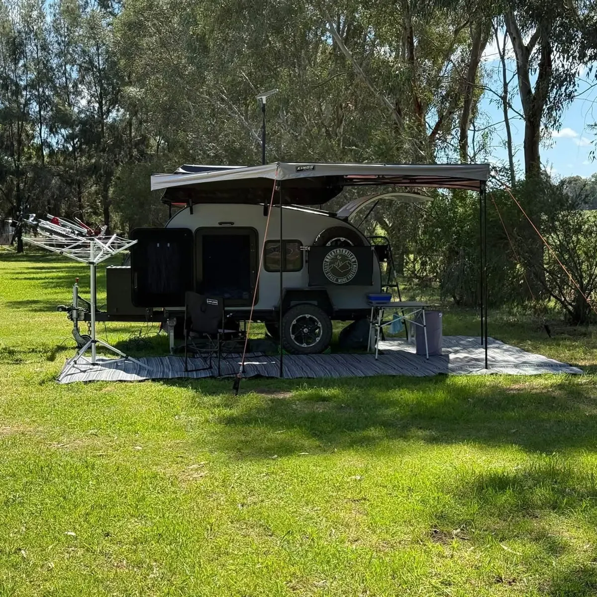 Michael’s Ultra at a green campsite beneath tall trees, with its awning open